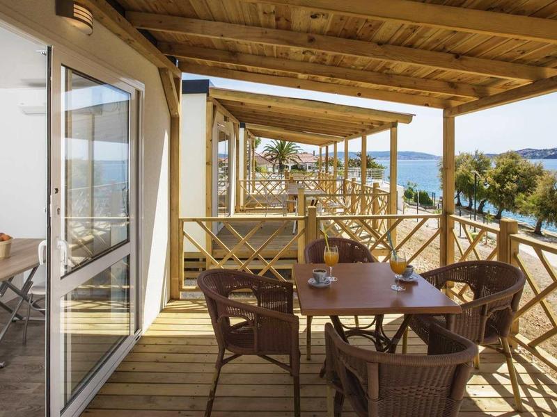 Balkon mit Holzgeländer und Sitzgruppe, Blick auf Meer und grüne Inseln im Hintergrund.