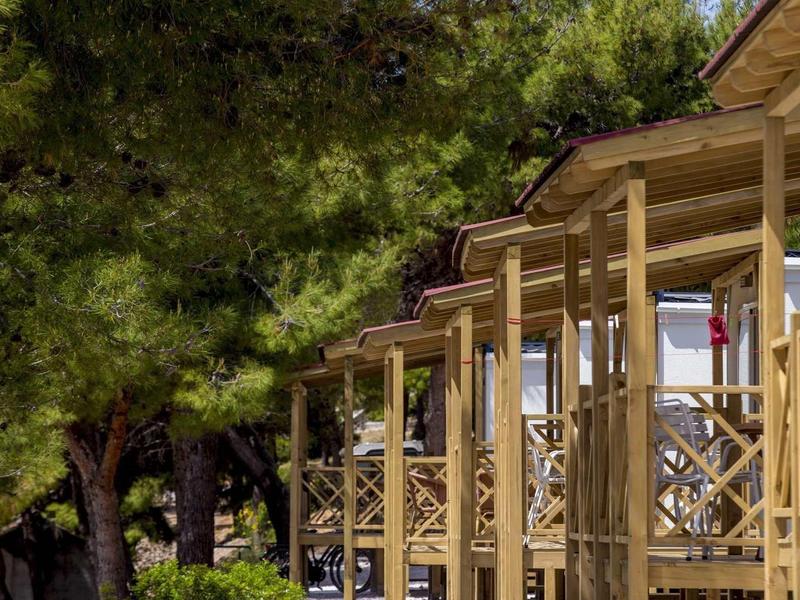 Reihe von Holzbalkonen an einem Haus, umgeben von grünen Bäumen bei Sonnenschein.