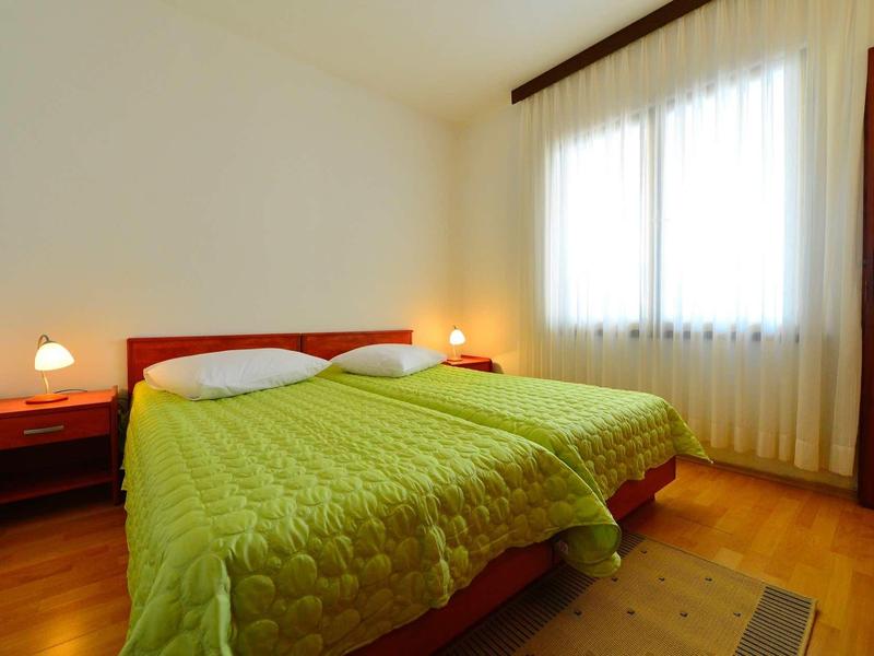 Ein helles Schlafzimmer mit zwei Betten, grüner Bettdecke, zwei Nachttischen und großen Fenstern.