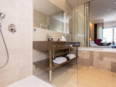 Modernes Badezimmer mit begehbarer Dusche, Glasabtrennung und Holzregal mit Handtüchern.