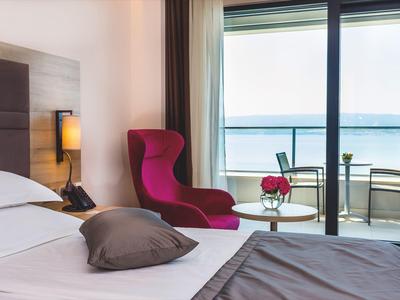 Modernes Hotelzimmer mit Bett, rotem Sessel und Balkon mit Meerblick.