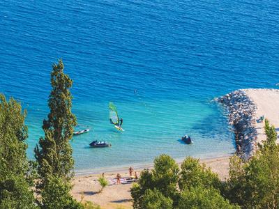 Vue sur une plage bleue calme avec des arbres et des personnes sur le rivage près d'un récif rocheux.