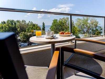 Balkon mit Tisch, Stühlen, Frühstück und Blick auf das Meer und Bäume.