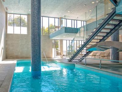 Piscine intérieure lumineuse avec eau bleue et escalier dans un intérieur d'hôtel moderne.