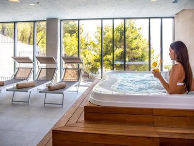 Frau entspannt im Whirlpool eines modernen Wellnessbereichs mit Liegestühlen und großen Fenstern.