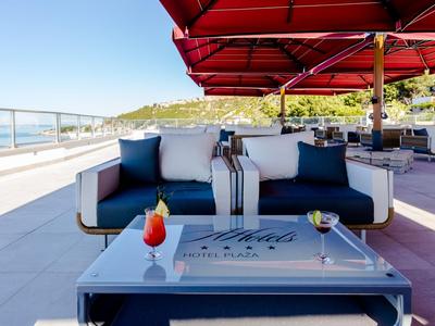 Canapé lounge moderne avec coussins et boissons sur terrasse d'hôtel ensoleillée avec vue sur la mer.