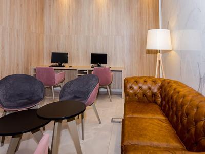 Espace d'attente d'hôtel moderne avec chaises, canapé, postes de travail et lampe sur pied.