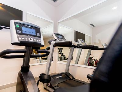 Salle de sport moderne avec tapis de course devant un mur miroir dans un hôtel.