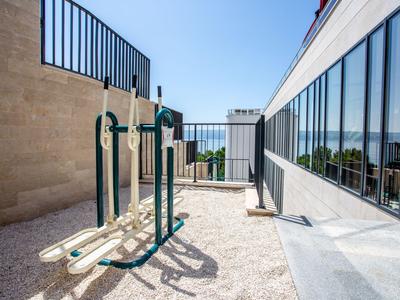 Équipements de fitness en plein air sur une terrasse ensoleillée à côté d'un bâtiment hôtelier moderne avec fenêtres en verre.