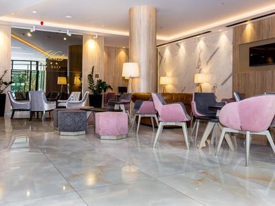 Espace lounge d'hôtel moderne avec fauteuils roses, chaises grises et sol en marbre.