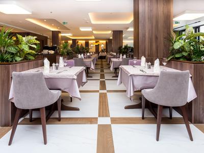Salle à manger moderne d'hôtel avec tables blanches, chaises grises et plantes vertes.