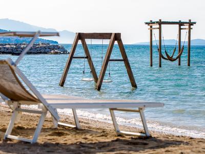 Leerer Liegestuhl am Sandstrand, Holzbalken mit Schaukeln im Meer, ruhiges blaues Wasser.