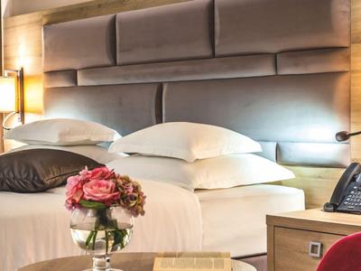 Chambre d'hôtel élégante avec grand lit, tête de lit rembourrée et vase de fleurs.