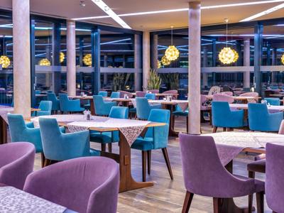 Restaurant d'hôtel moderne avec des chaises colorées et des tables élégantes sous des suspensions chaudes.