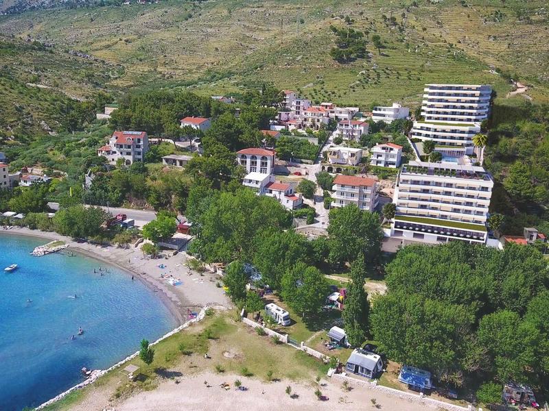 Hotelanlage und Strand an einer Küste mit grünem Hügel im Hintergrund.