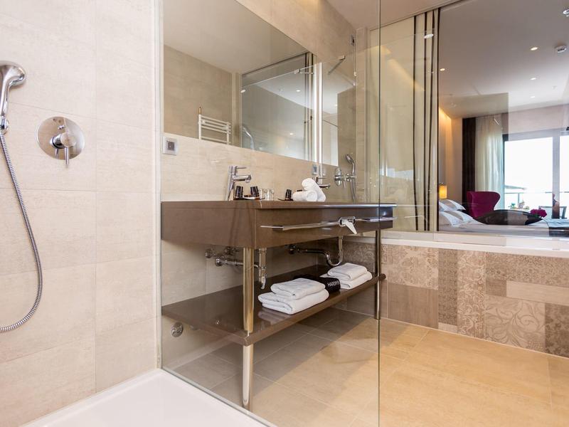 Modernes Badezimmer mit begehbarer Dusche, Glasabtrennung und Holzregal mit Handtüchern.