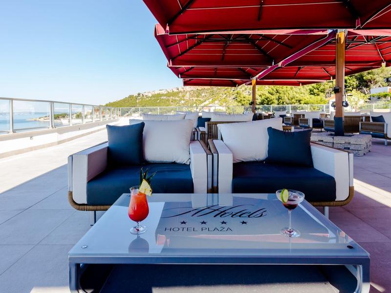 Moderner Sitzbereich mit Getränken und rotem Sonnenschirm auf einer Terrassenlounge mit Meerblick.