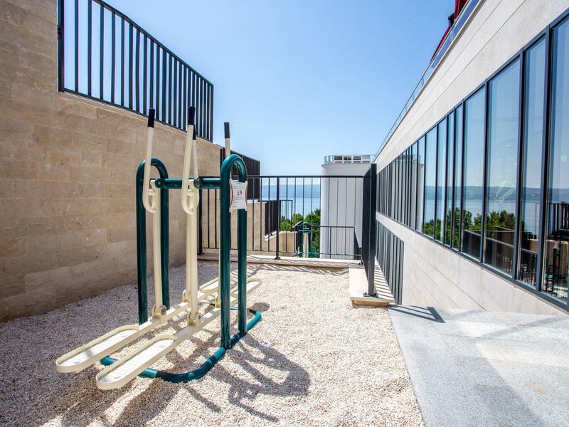 Außenbereich mit Fitnessgeräten neben einem modernen Hotelgebäude unter blauem Himmel