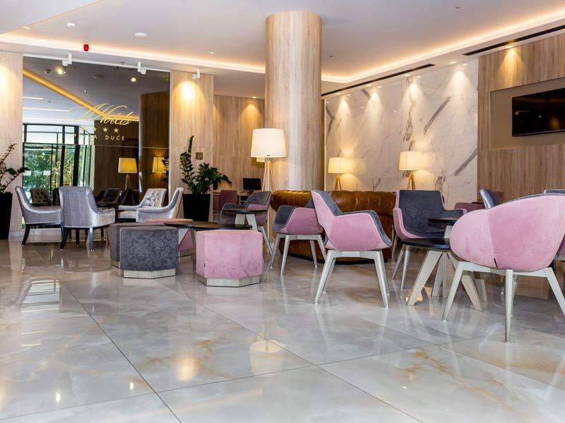 Moderner Hotel-Lobbybereich mit rosa Sesseln, grauen Sofas und stilvoller Beleuchtung.