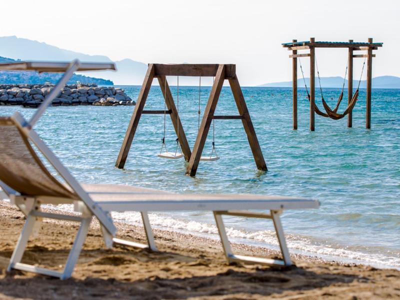 Leerer Liegestuhl am Sandstrand, Holzbalken mit Schaukeln im Meer, ruhiges blaues Wasser.