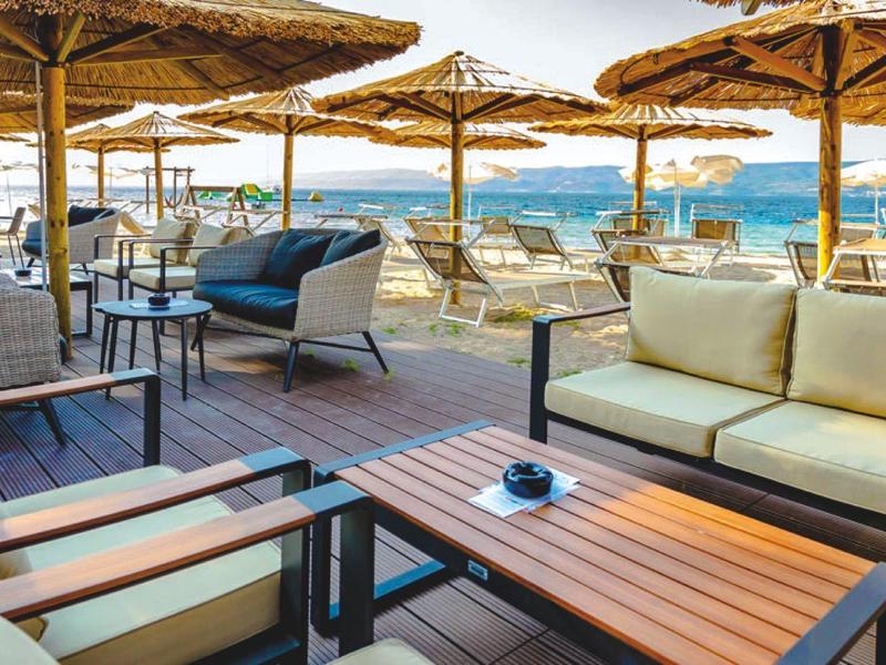 Outdoor-Lounge mit Sofas unter Schirmen und Meerblick bei sonnigem Wetter.