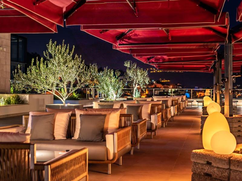 Dachterrasse mit bequemen Sitzgruppen und warmem Licht unter roten Markisen bei Nacht.