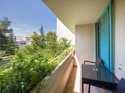 Balcone con tavolo e due sedie con vista su giardino verde e edificio sotto un cielo limpido.