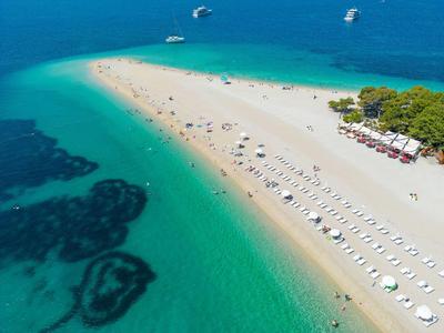 Vista aerea di una spiaggia sabbiosa con ombrelloni e acqua turchese cristallina.
