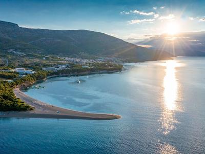Tramonto su costa calma con montagne sullo sfondo e acqua limpida riflettente.