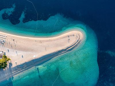 Veduta aerea di una barra di sabbia con lettini prendisole circondata da acqua blu chiara
