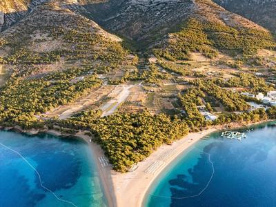 Punta sabbiosa con scogliere, colline boschive e acqua blu cristallina lungo la costa