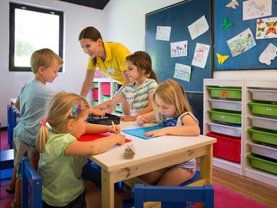 Bambini che dipingono a un tavolo in una stanza luminosa e colorata con una lavagna e scaffali.