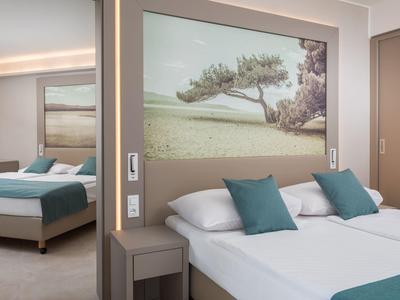 Camera d'hotel moderna con letto matrimoniale, cuscini verdi e immagine naturale rilassante sulla parete.