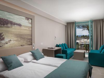 Camera d'hotel moderna con letto matrimoniale, sedie blu e vista sulla terrazza e sul mare.