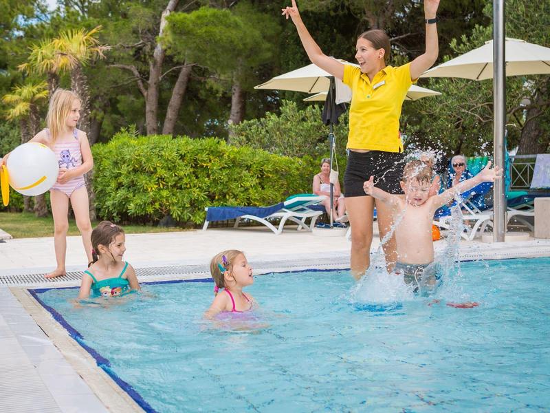 Bambini e adulti che giocano e schizzano in una piscina all'aperto di un hotel in una giornata di sole.