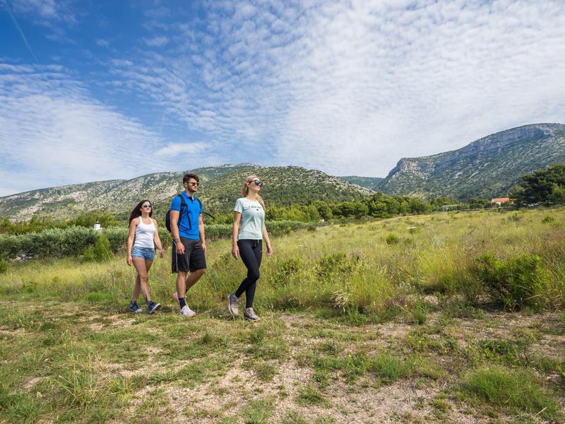 Tre escursionisti camminano su un sentiero attraverso prati selvaggi con montagne sullo sfondo.