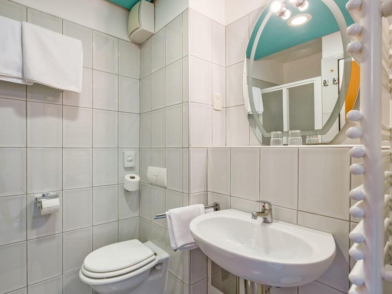 Piccolo bagno con wc bianco, lavabo e asciugamani in pareti piastrellate moderne.