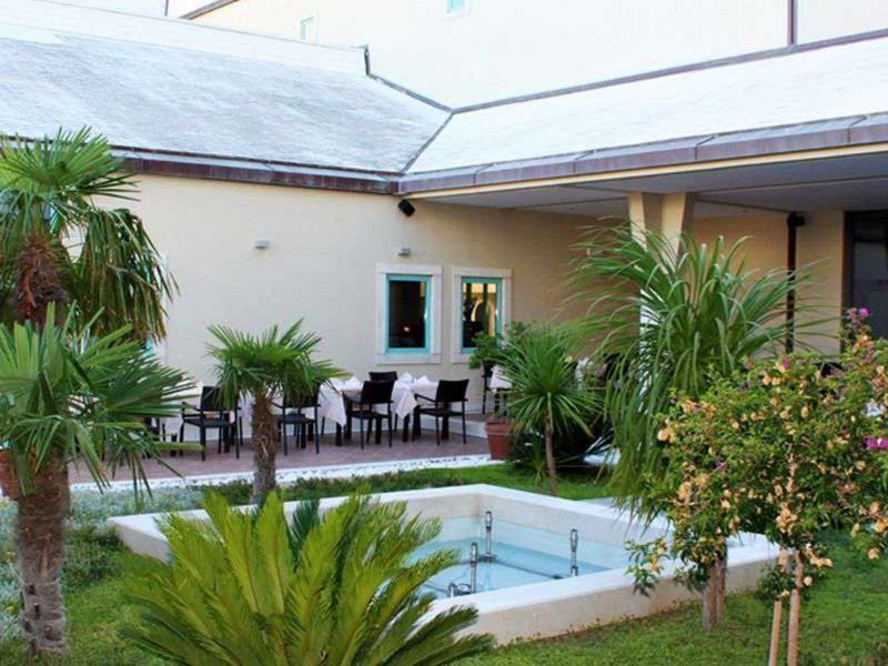 Cortile dell'hotel con piscina, tavoli e sedie circondati da piante tropicali.