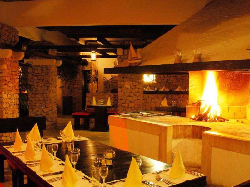 Interno accogliente con camino, tavoli in legno e tovaglie bianche in un ristorante rustico.