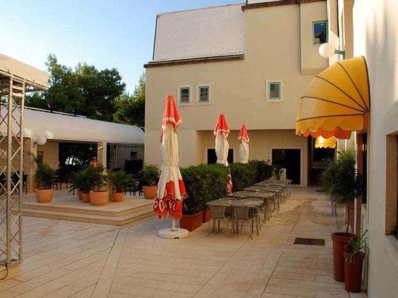 Terrazza d'hotel con tavoli, ombrelloni rossi chiusi e decorazioni gialle e verdi.