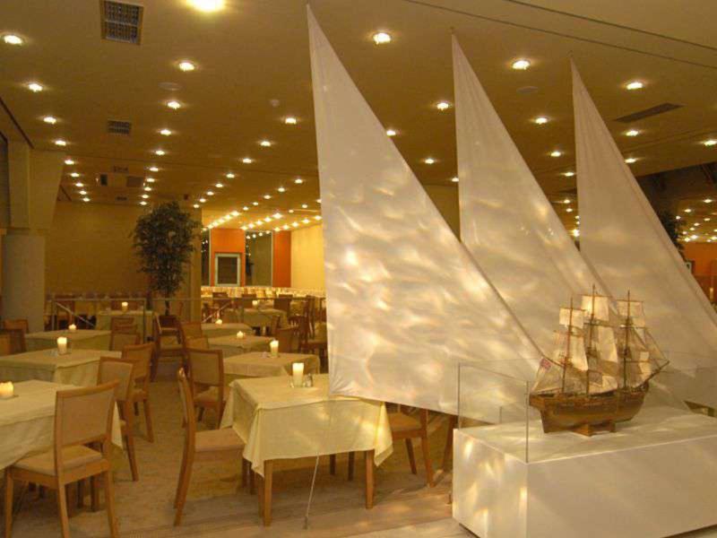 Interno di un ristorante illuminato con un grande modello di barca a vela bianca in primo piano.