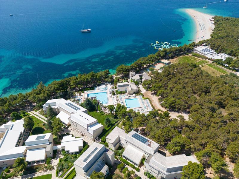 Complesso turistico con diversi edifici moderni, piscine e accesso a una spiaggia di sabbia bianca vicino a un'acqua azzurra e limpida.