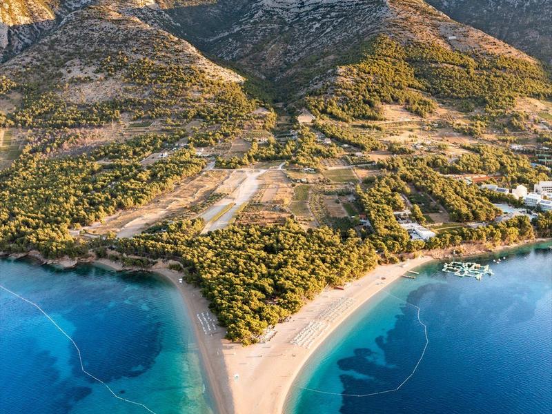 Punta sabbiosa con scogliere, colline boschive e acqua blu cristallina lungo la costa