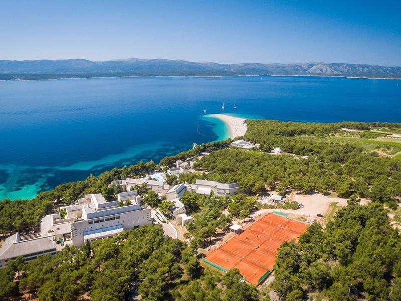 Vista aerea di un resort con campi da tennis e una lunga spiaggia sabbiosa vicino al mare.