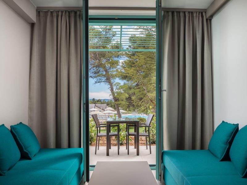 Vista da una stanza con divani blu su una terrazza con tavolo e sedie di fronte alla natura verde.