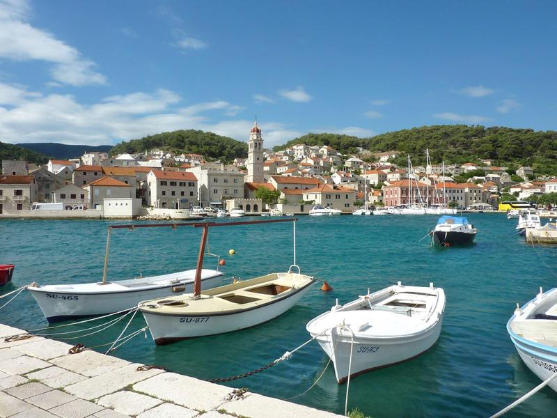 Piccolo porto turistico con barche sull'acqua turchese e case sullo sfondo.