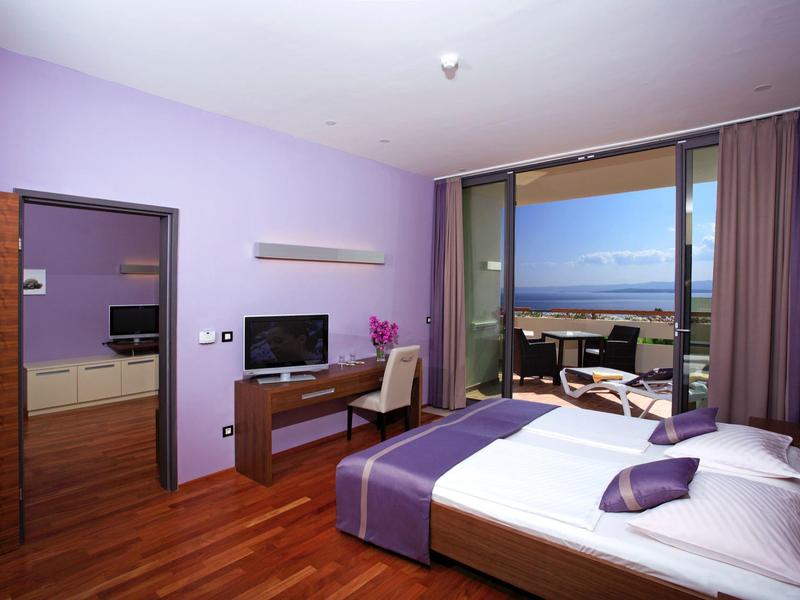 Camera d'hotel moderna con letto matrimoniale, scrivania, TV e balcone con vista mare.