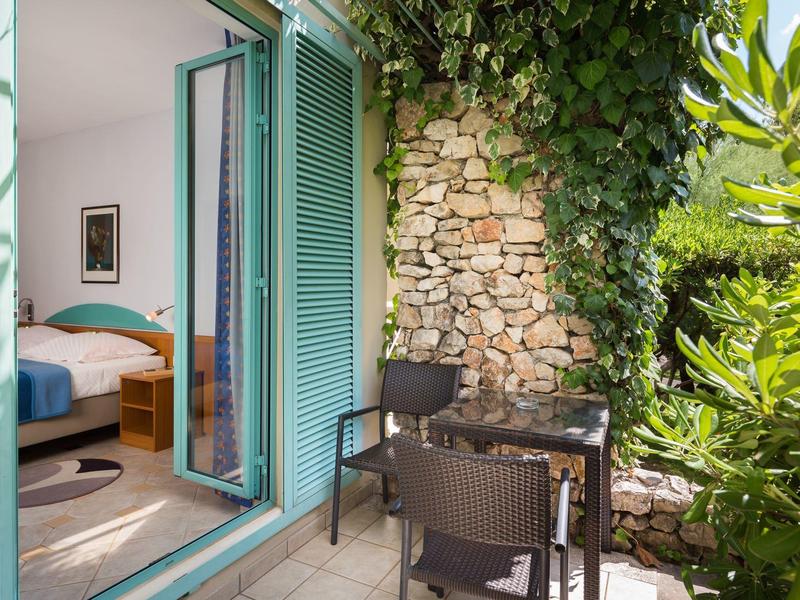 Accogliente balcone con tavolo e sedie accanto a finestra aperta con vista su vegetazione rigogliosa.