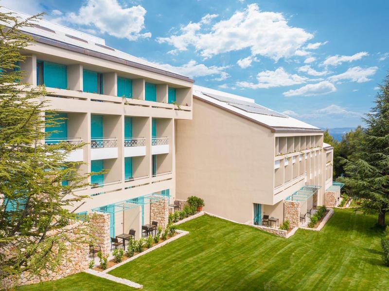 Edifici di hotel moderni con balconi e prato verde curato sotto un cielo azzurro.