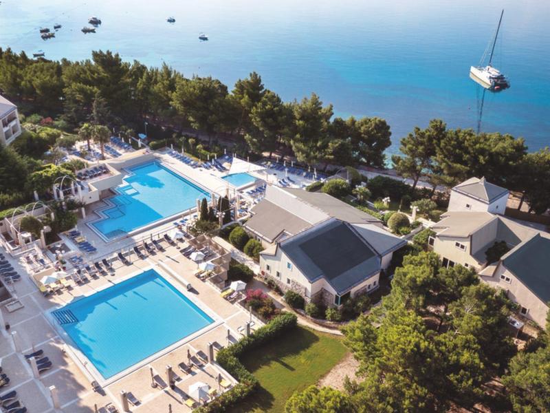 Complesso alberghiero con due piscine all'aperto, lettini e vista sul mare con una barca a vela.